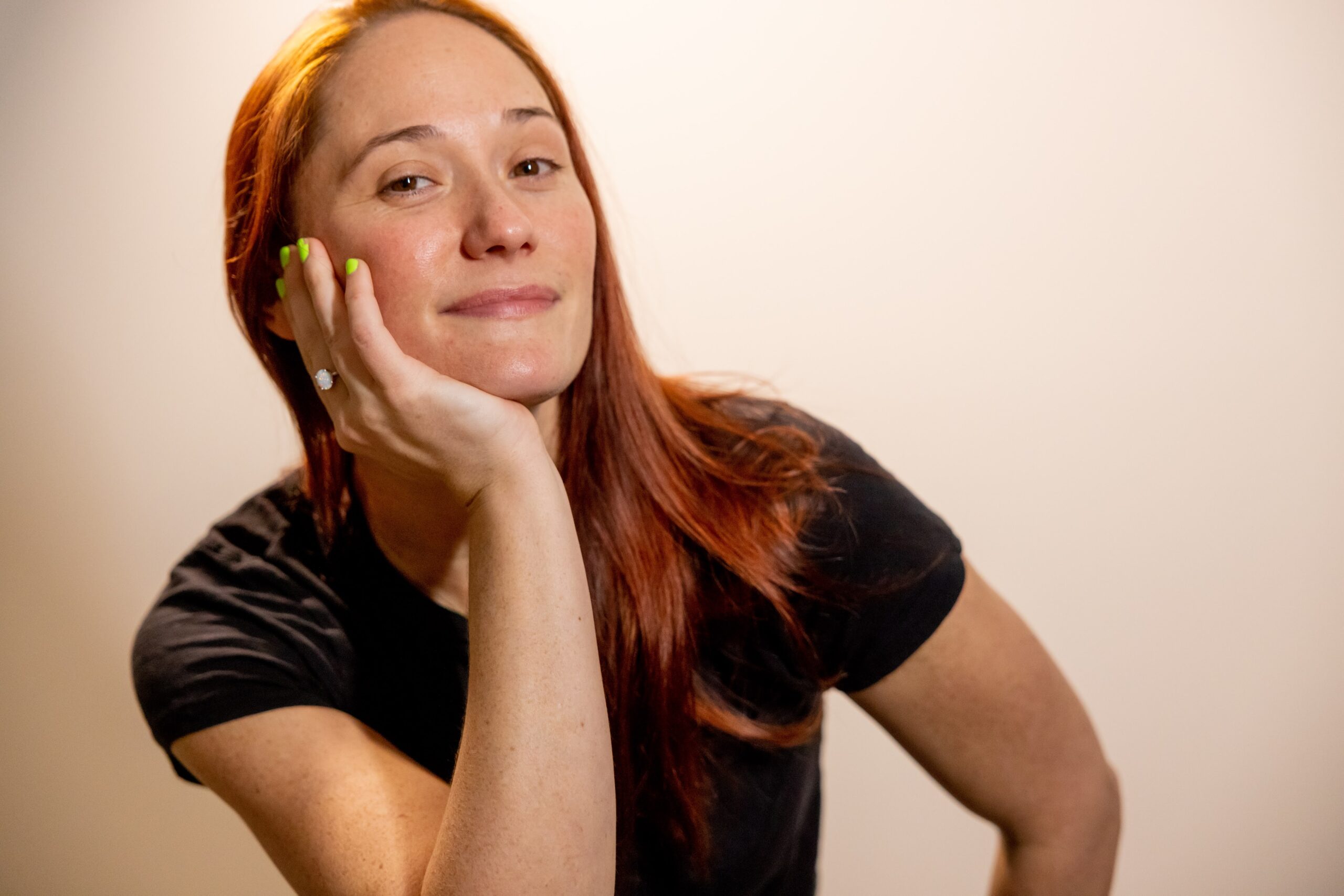 Sarah Brown, woman with long red hair, wearing a black tee-shirt, with head propped on chin smiling slightly at the camera